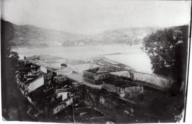 Las casas de la calle del Pozo adosadas a la muralla del frente de tierra. En esta imagen, anterior a 1863, se aprecian la parte superior de esta colosal fortificación así como, más adelante, el semibaluarte de Santiago.
Foto del álbum de Fco. López Alén. 
