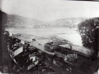 Parte superior de la cortina del Frente de Tierra, entre el semi baluarte de Santiago, del que se aprecia una parte delante de la muralla, y el Cubo Imperial. Las casas adosadas a la muralla pertenecían a la Calle del Pozo, y fueron unas de las pocas que se salvaron del incendio. En este paseo de ronda se produjeron atroces escenas de guerra, además de la explosión que ocasionó la caída de la plaza.
Foto Colecc. Fco. López Alén.
