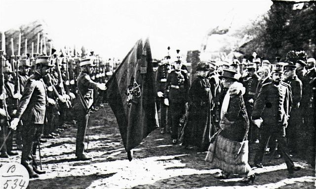 Momento en que la reina Victoria Eugenia saluda la bandera del regimiento Sicilia. Detrás puede verse a la reina María Cristina.